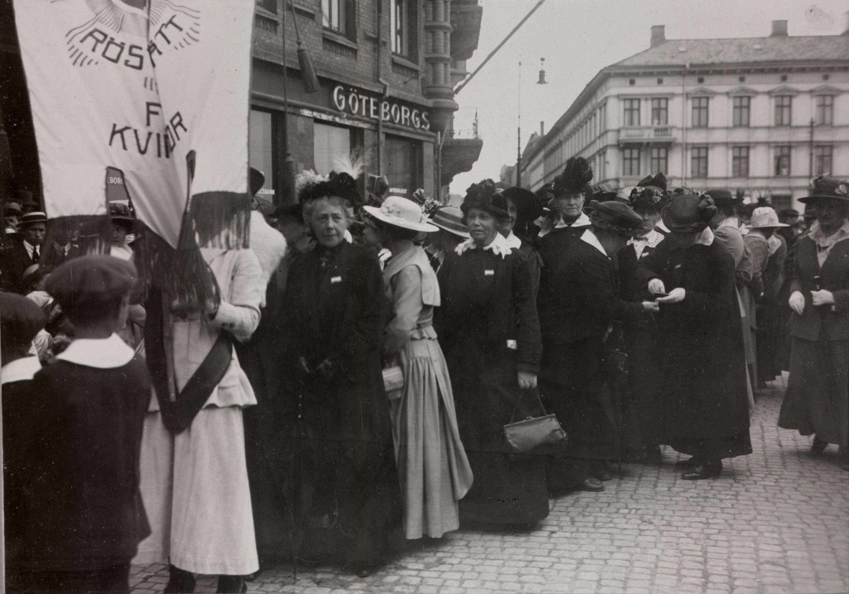 Kvinnor i demonstrationståg i Göteborg med en fana som bär orden Rösträtt för kvinnor.