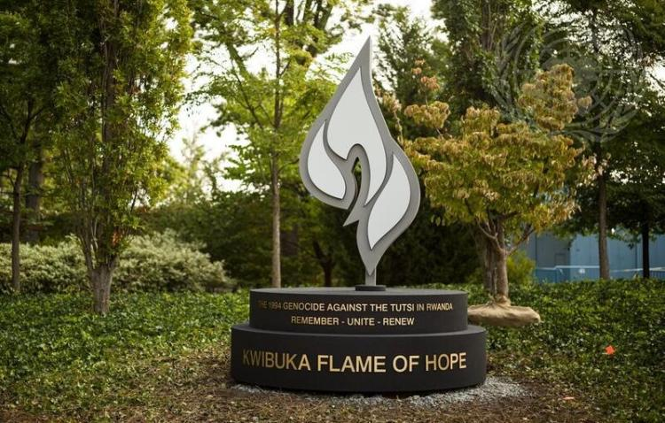 Minnesmärke med texten Kwibuka Flame of Hope, en stiliserad låga i en grönskande park.